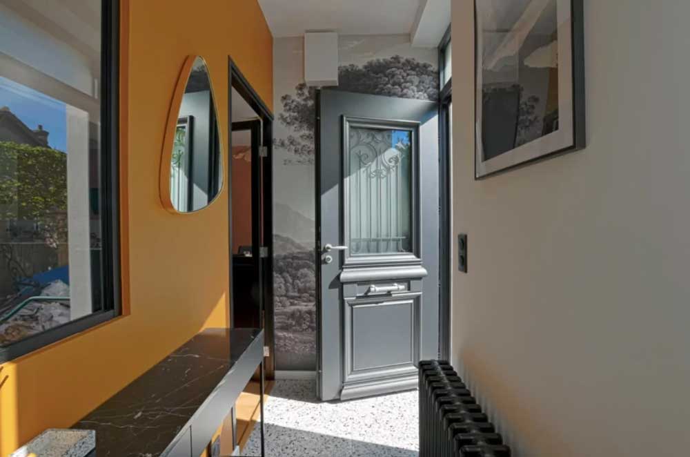 couloir d'entrée colorée en jaune, avec une porte d'entrée vitrée de style classique ouverte