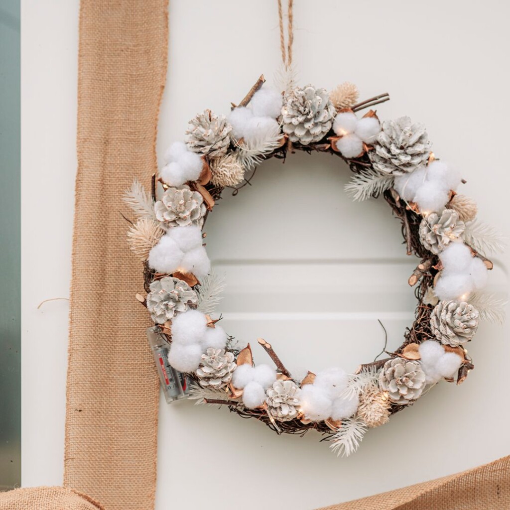 zoom sur une couronne de noel avec des fleurs de cotons, des leds et des pommes de pins sur une porte d'entrée