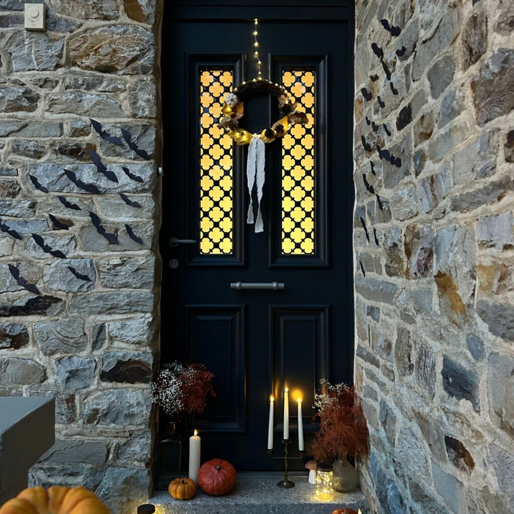 porte d'entrée bel'm décorée pour halloween avec des chauves souris sur les murs, une couronne automnale et d'autres décorations