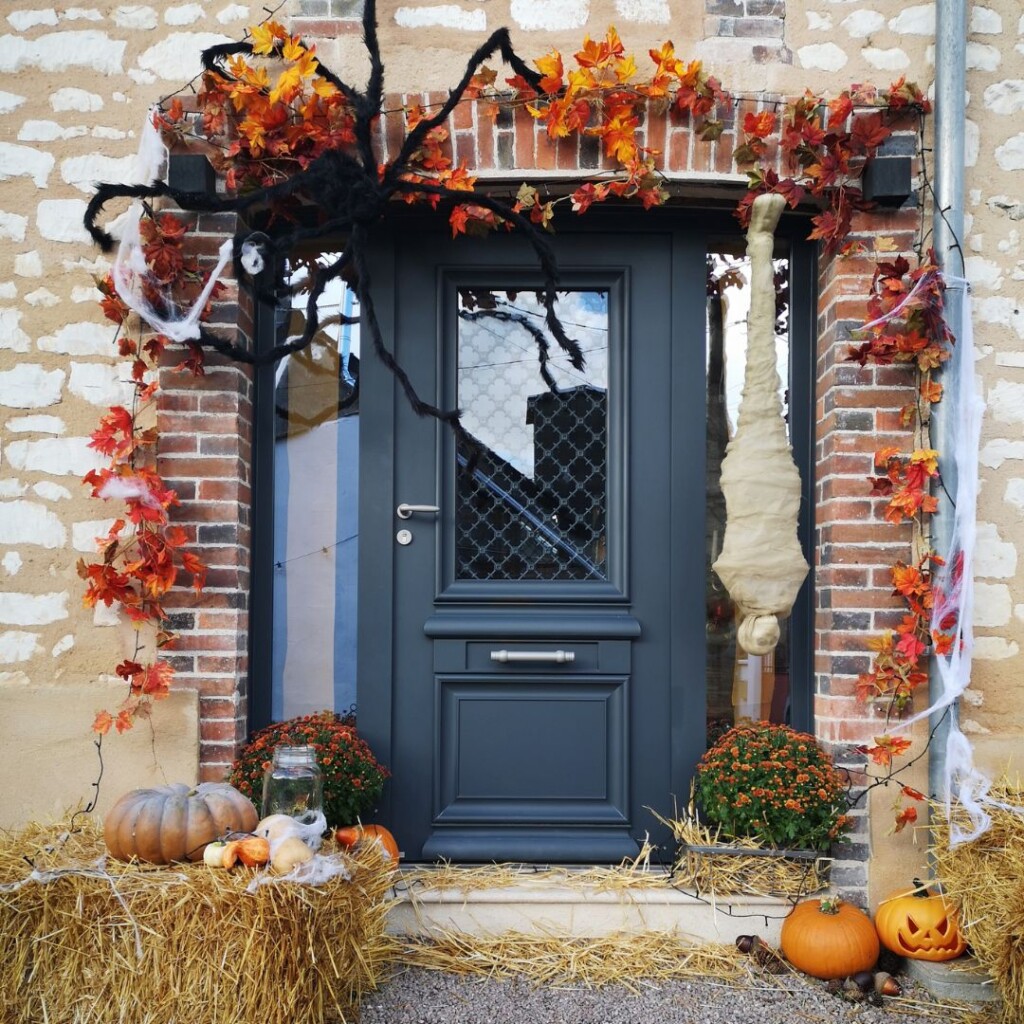 extérieur de maison décoré pour halloween avec des feuilles oranges, des courges, un araignée et d'autres accessoires