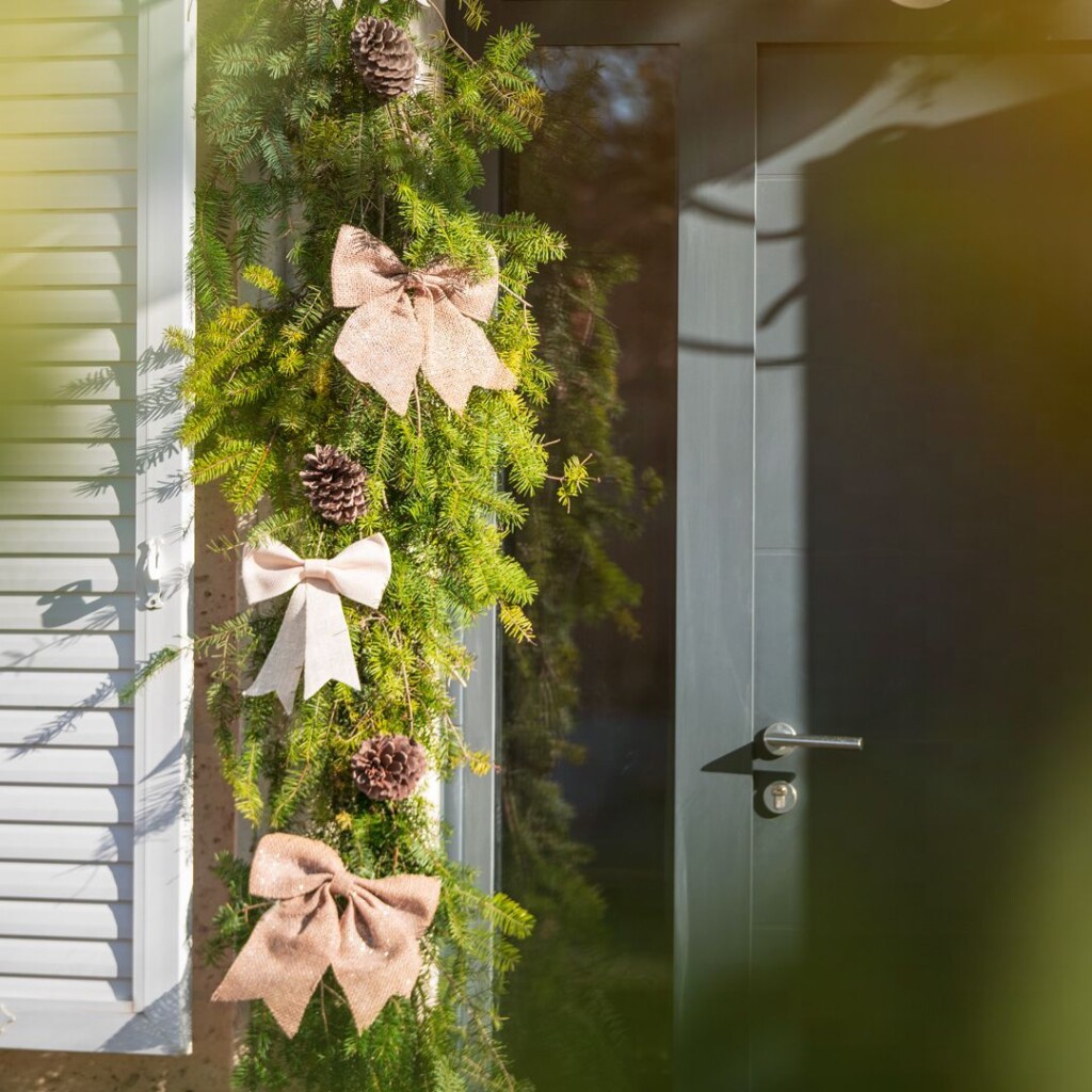 zoom sur une décoration autour d'une porte d'entrée avec des branches de sapin, noeud et pomme de pin