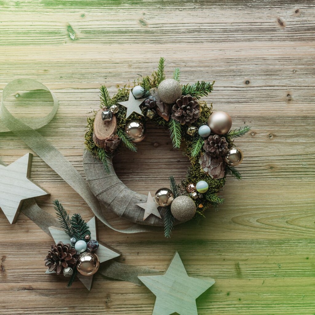 diy d'une couronne de noel pour porte d'entrée avec du sapin, des pommes de pins, des boules de noel et du ruban