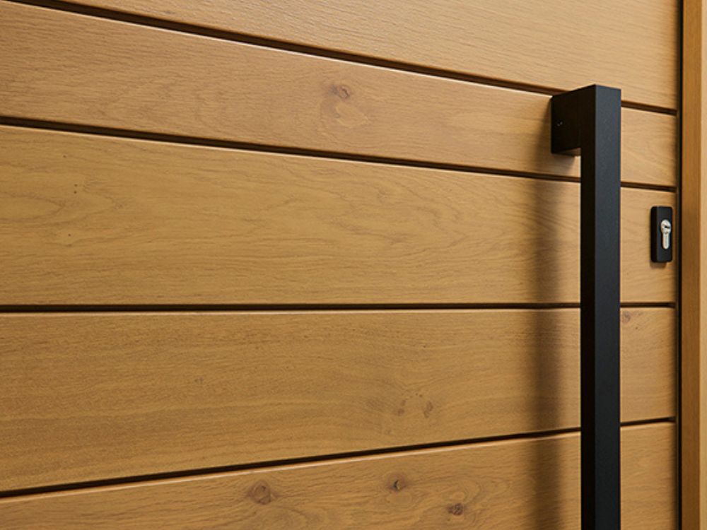 zoom sur une barre de tirage noire contemporaine d'une porte d'entrée en chene